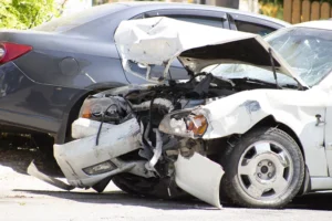 A white car with heavy front-end damage is parked next to a dark gray car with minor scratches on its rear side; both vehicles appear to be involved in a collision.