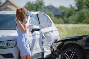 A woman stands beside two damaged cars after a collision, talking on her phone and gesturing with her hand.