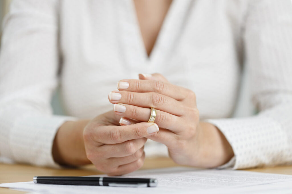 A person wearing a white shirt is removing a gold ring from their finger, with a pen and document on the table in front of them.
