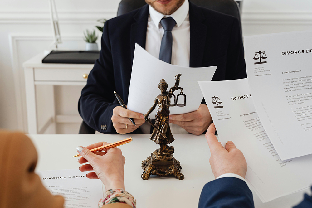 Two people holding divorce documents sit across from a person in a suit, with a Lady Justice statue on the desk between them.