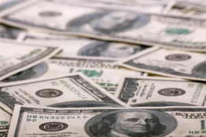 Several U.S. one hundred dollar bills are scattered in a pile, displaying Benjamin Franklin’s portrait and other recognizable security features.