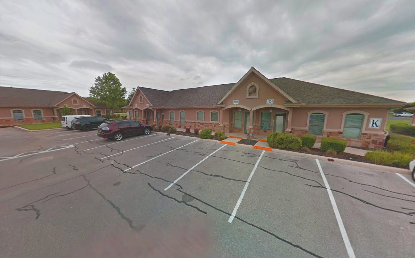 A single-story brick office building with several parking spaces in front, some of which are empty, on a cloudy day.