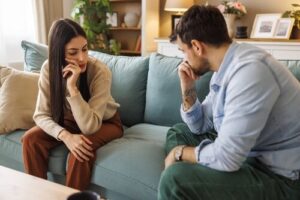 Young couple sitting apart on sofa during heated argument at home