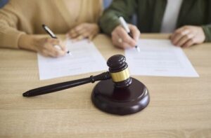 two individuals signing legal documents beside courtroom gavel on desk