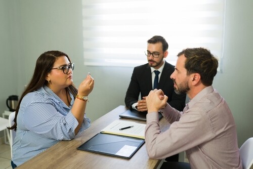 couple meeting with suited attorney at desk with legal documents and clipboard